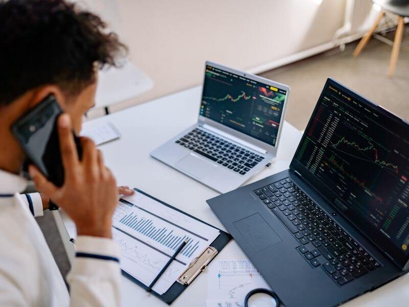 Person on a phone call at a desk with laptops showing stock charts